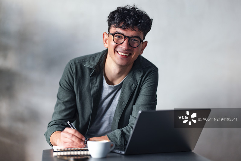 年轻专业人士在咖啡馆里微笑着使用笔记本电脑和笔记本工作图片素材