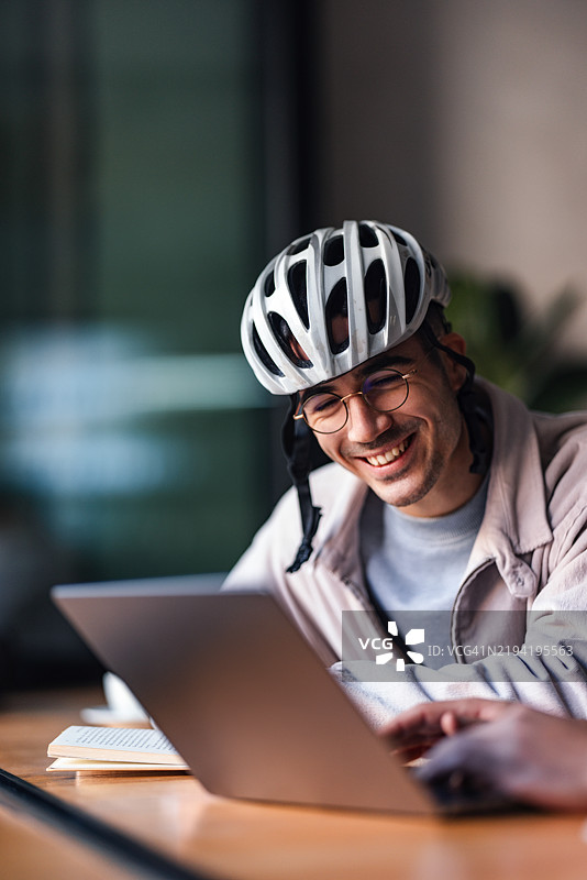 戴着头盔的男子在休闲环境中微笑着使用笔记本电脑图片素材