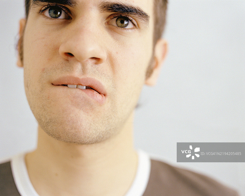 年轻男子咬着嘴唇，摄影棚照片图片素材