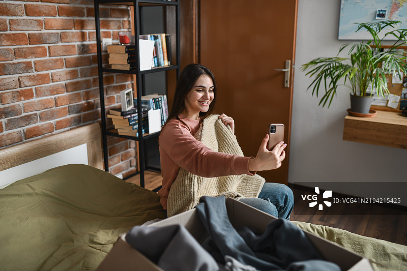 快乐的女性穿着新毛衣自拍，发给朋友听取她的意见。图片素材