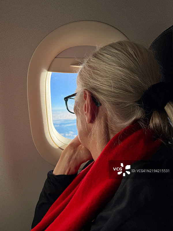 一位老年女性坐在飞机上，望着窗外。图片素材