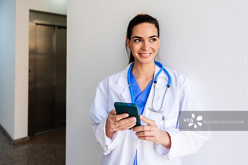 微笑的医生在医院走廊使用智能手机图片素材