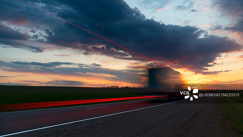 模糊的卡车在高速公路上高速行驶，明亮的黄色红色日落，货物运输。图片素材