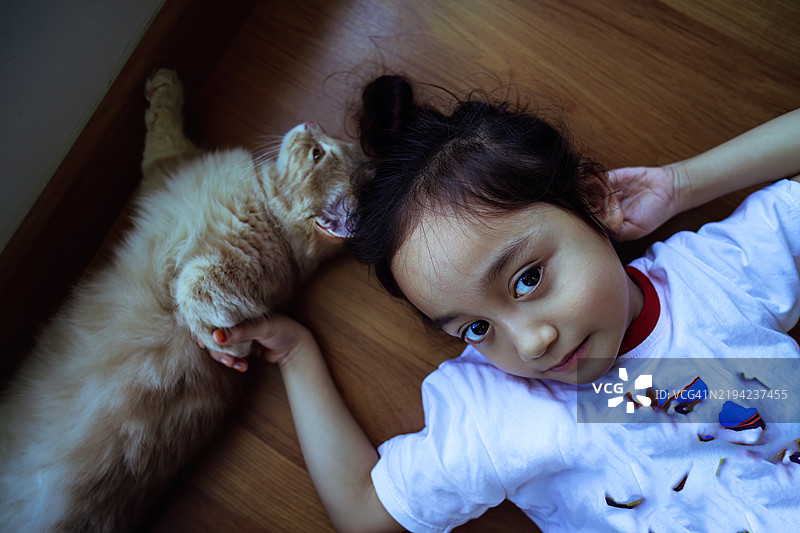 小女孩和她的小猫在地板上放松，俯视角度。图片素材