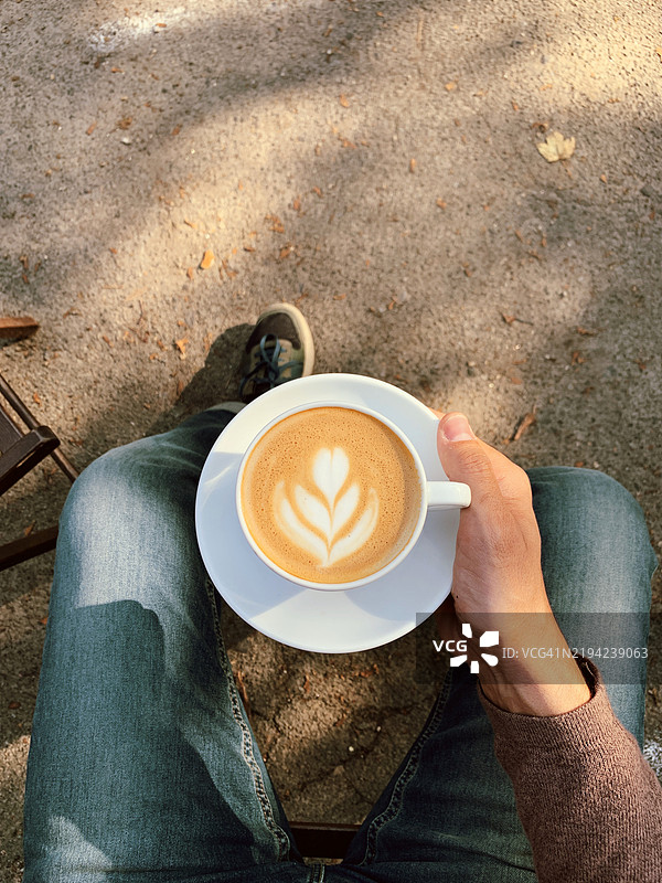 男人坐着，手里拿着一杯卡布奇诺，从个人视角看。图片素材