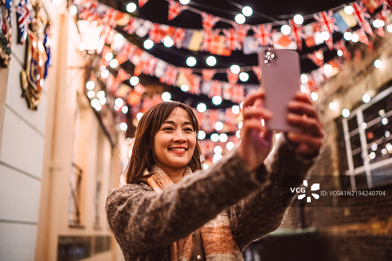 快乐的女性游客在旅行中，在节日灯光下用智能手机自拍图片素材