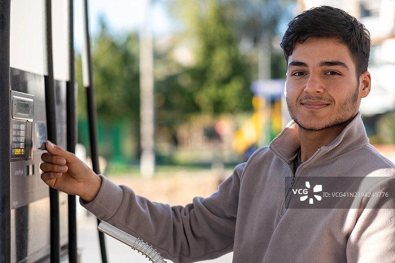 年轻男子在加油站使用非接触式支付方式支付燃料费用图片素材