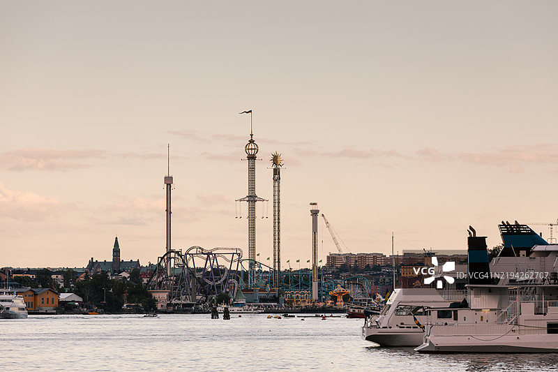 黄昏时分的游乐园，位于被水环绕的大城市中。图片素材