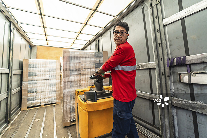 专注的拉丁裔男性工人在配送仓库装载送货卡车的背影图片素材