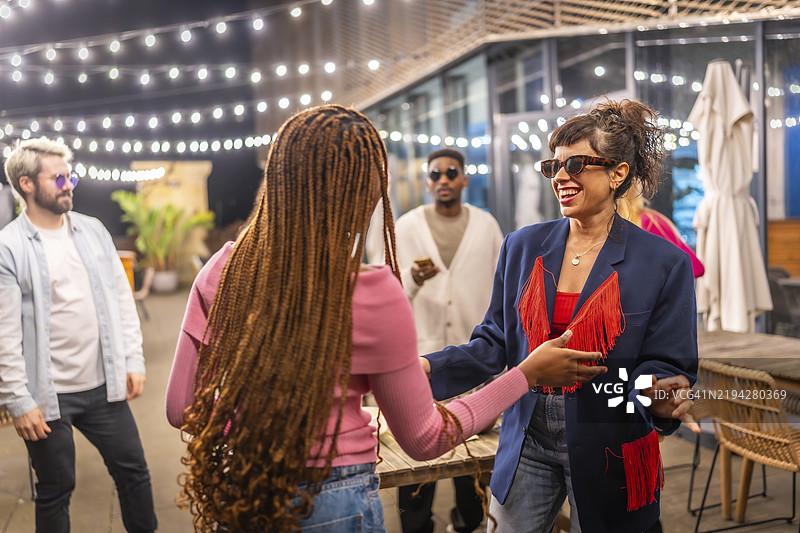两个多民族的女性朋友在户外夜晚派对上与其他朋友一起跳舞图片素材