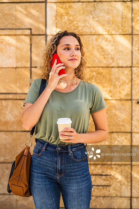 年轻女性一边喝咖啡一边打手机。图片素材
