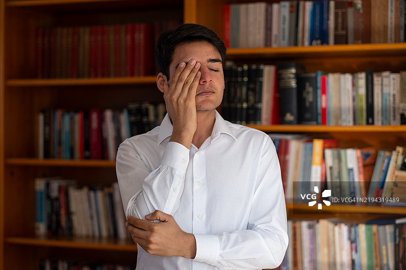 在图书馆里捂住眼睛的压力大的年轻学生图片素材