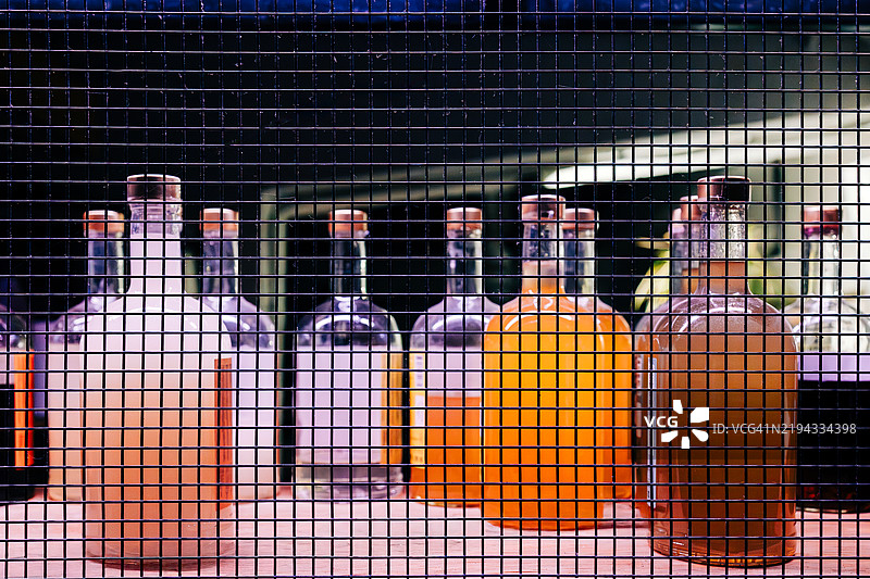 五颜六色的酒精饮料装在玻璃瓶中，背景是金属网格。图片素材