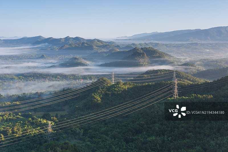 晨雾笼罩着山脉上的高压电力输送塔。图片素材