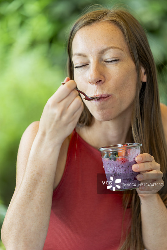 成熟的女性在阳光明媚的夏日享用健康早餐，餐桌上有酸奶和超级食品水果。图片素材