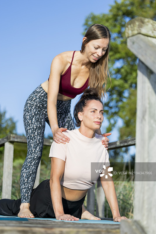 年轻、美丽的中年女性在阿默湖旁的码头上与她的女性私人瑜伽教练一起练习瑜伽图片素材