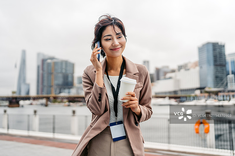 年轻的亚洲女商人在澳大利亚悉尼达令港一边喝外带咖啡一边打电话图片素材