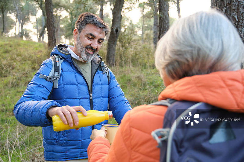 老年男子在徒步旅行中为女子倒热饮。图片素材