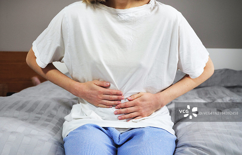 年轻的金发女性坐在家里的沙发上，感到腹部疼痛。图片素材