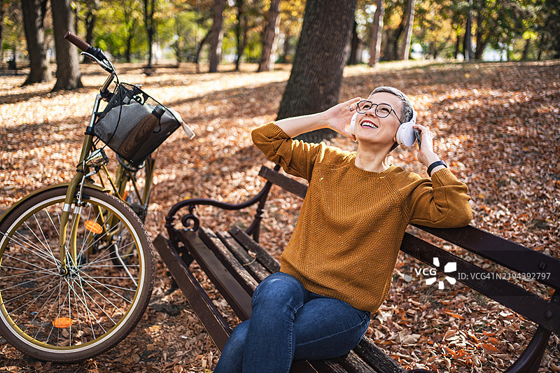快乐的女人在公园里骑自行车后，戴着耳机听音乐图片素材