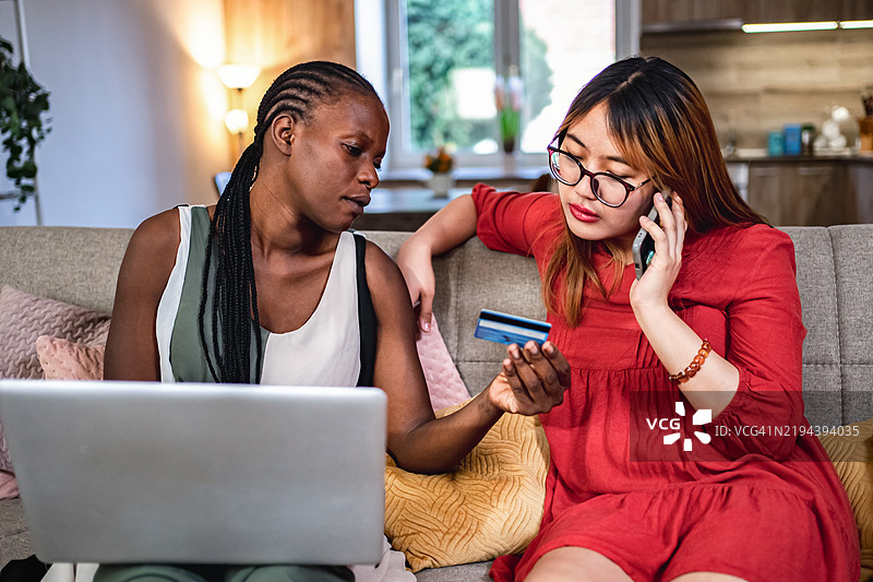 两位年轻女性在家中使用笔记本电脑和信用卡进行在线购物图片素材