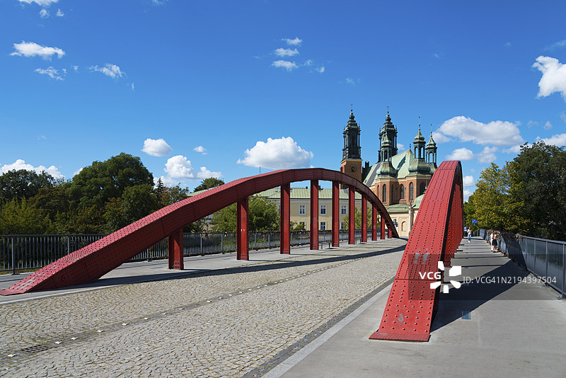 一座现代红色桥梁通向背景中的大教堂,蓝天白云映衬下的圣彼得和圣保罗使徒大教堂,乔丹主教桥,波兹南,波兰大波兰省,欧洲图片素材