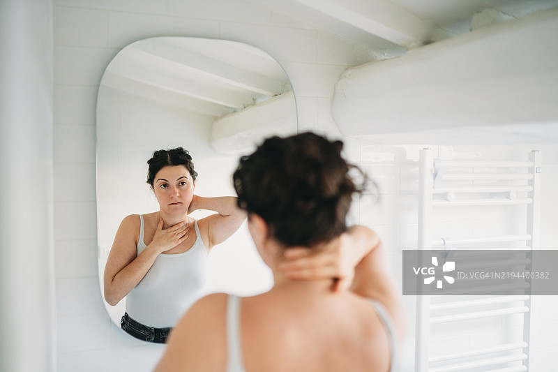 年轻女性在浴室镜子前检查自己的脖子图片素材