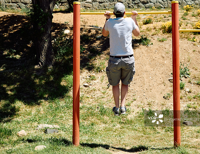 年轻小伙子在公园的横杆上做引体向上图片素材