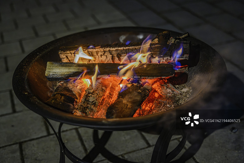在黑暗的鹅卵石上，火碗中燃烧的木材，夜晚温暖的火焰图片素材