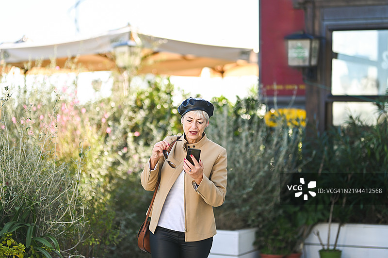 一位老年女性在城市中走路时使用智能手机图片素材