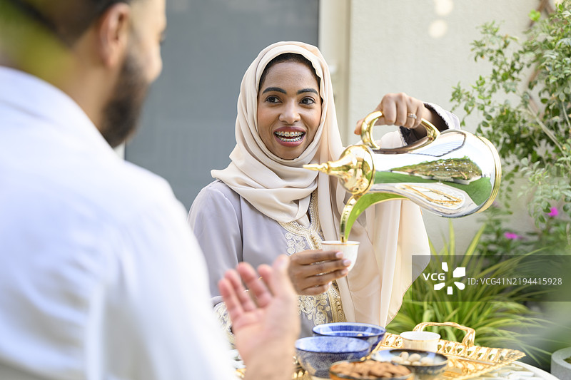 一位快乐的阿联酋女性微笑着从华丽的茶壶中倒阿拉伯茶图片素材