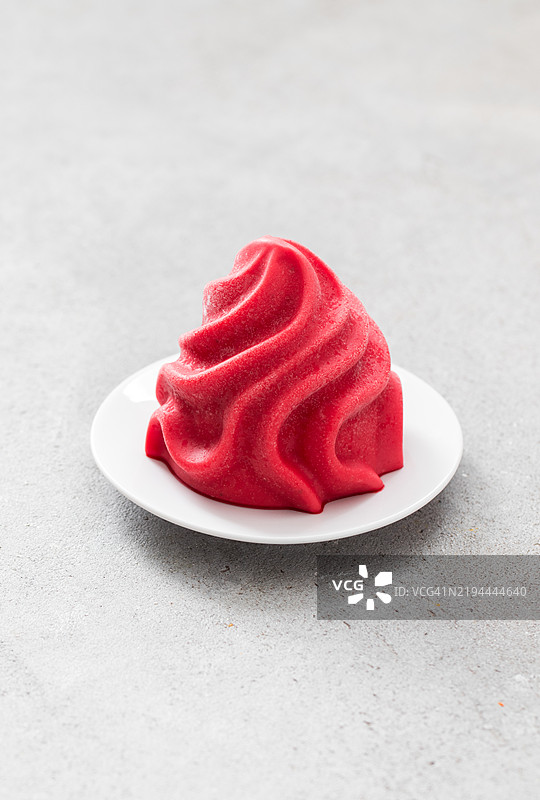 素食草莓冰沙，呈法式香草奶油的形状。放在盘子里。浅灰色背景。特写。图片素材