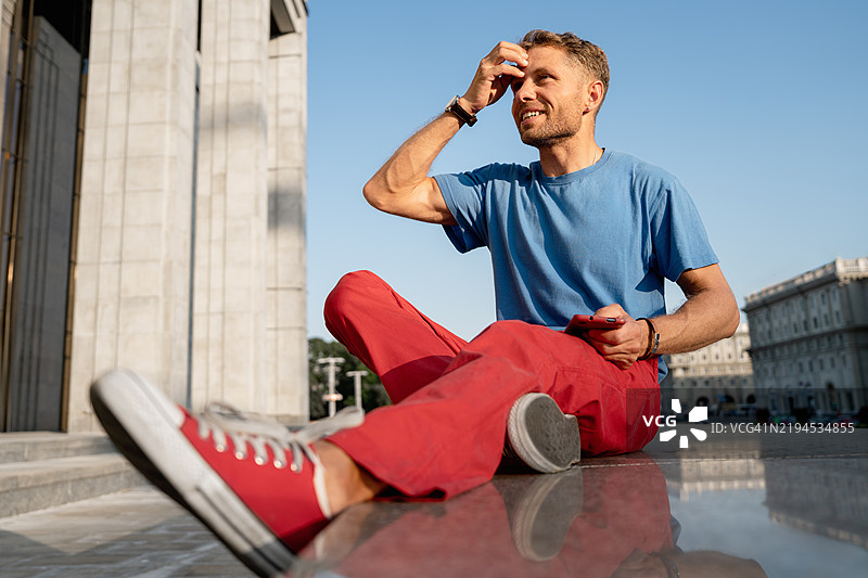 穿着蓝色T恤和红色裤子的成熟男子坐在城市的台阶上图片素材