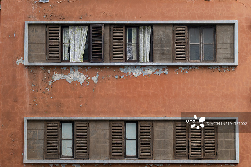 带木百叶窗的窗户，位于风化的橙色墙壁上图片素材