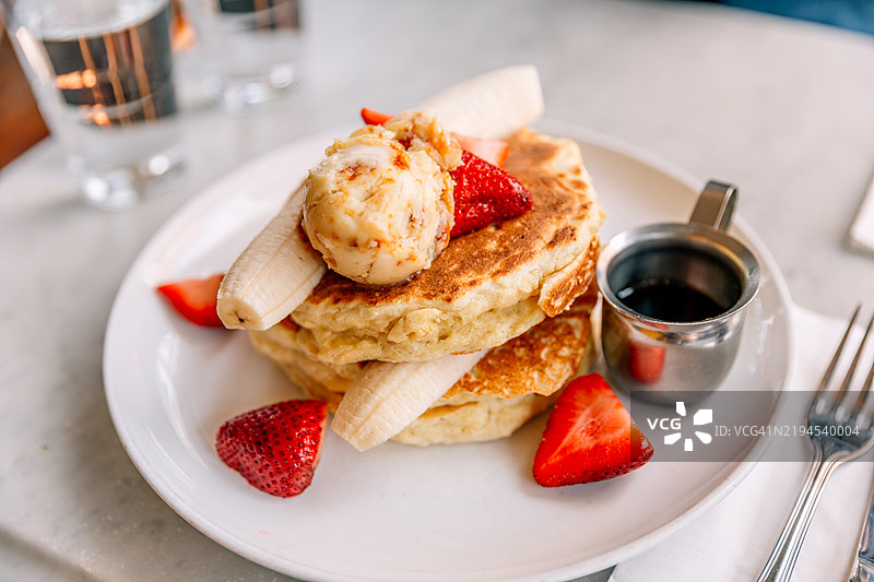 餐厅里近距离拍摄的煎饼，配有香蕉、草莓、黄油和枫糖浆图片素材