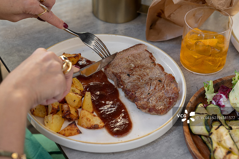 一位女性在餐厅里享用牛排，配有肉汁和土豆。图片素材