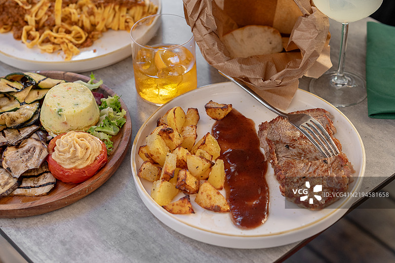 一位女性在餐厅里享用牛排，配有肉汁和土豆。图片素材