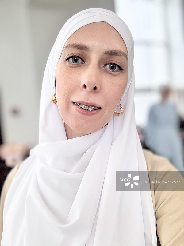 一位年轻穆斯林女性的自拍，她戴着牙套，头上裹着白色头巾。图片素材