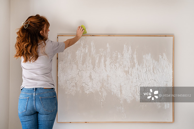 女人在墙上清洁大型抽象画的灰尘图片素材
