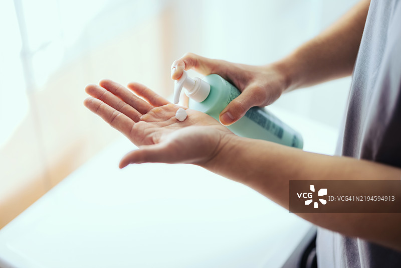 在明亮环境中用瓶子涂抹护肤乳液的手部图片素材