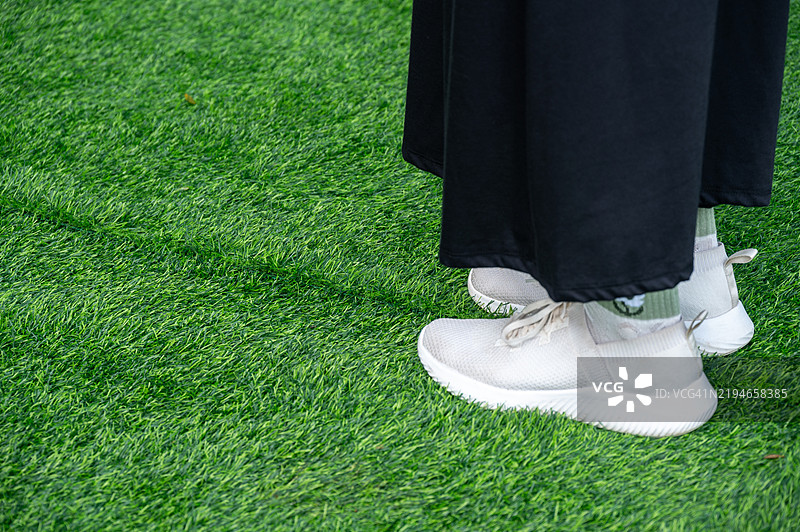 在运动场或花园中，某人站在未完成的绿色人造草坪上的特写镜头。图片素材