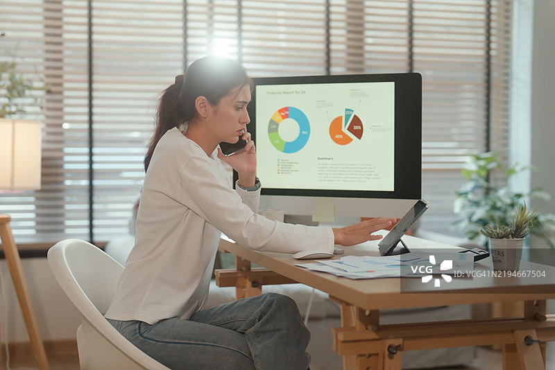 在家办公室中，女商人一边打电话一边使用平板电脑，屏幕上显示着财务数据。图片素材