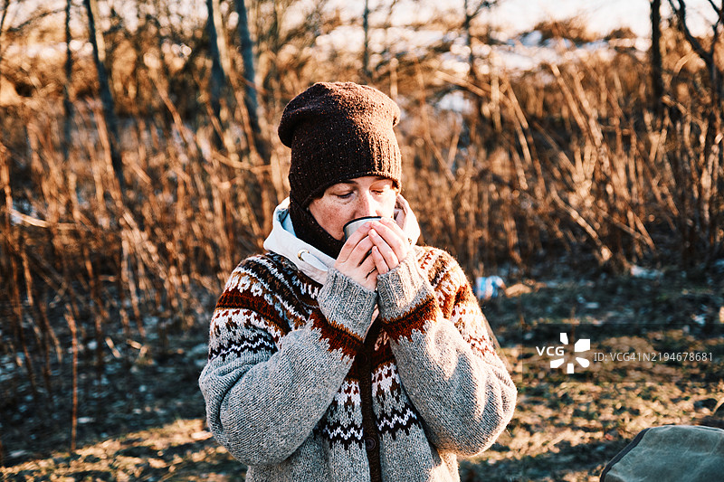 50岁的女性，热爱背包旅行，在寒冷阳光明媚的冬日河岸边品尝热茶。图片素材