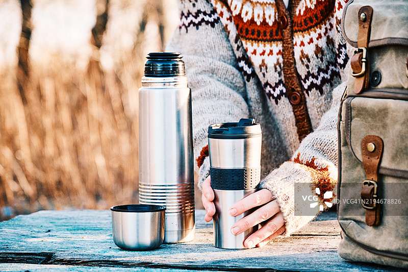 寒冷的沙漠风景，50岁的女性背包客在河岸边品尝热茶图片素材