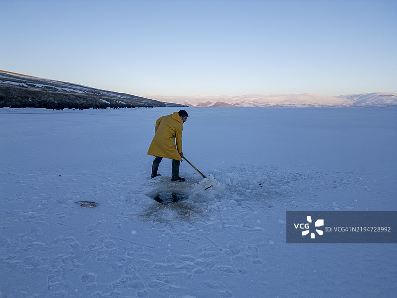 渔民在冰冻湖面上破冰以进行冰钓图片素材