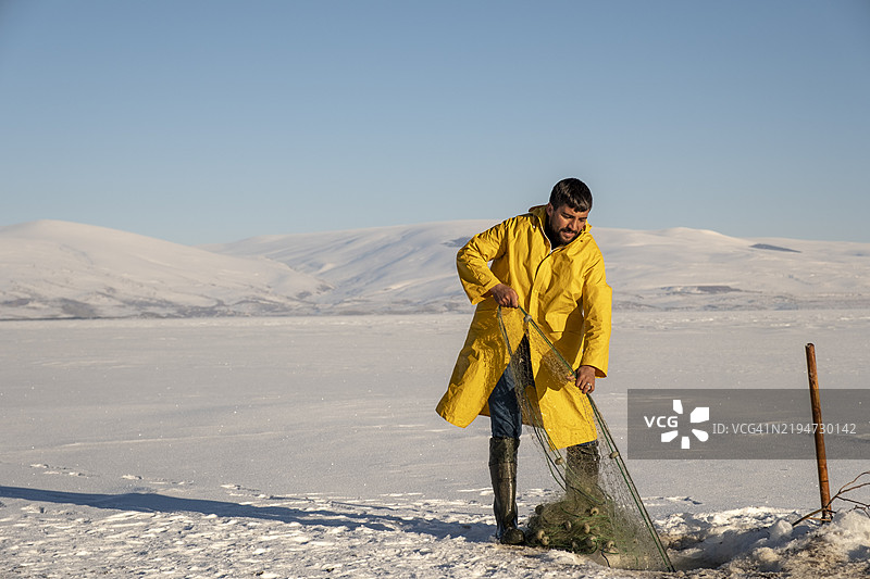 渔民从冰冻湖面钻孔中拉出渔网图片素材