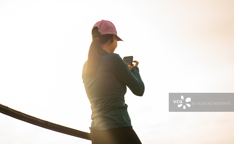 年轻女性背对着镜头在日出时用手机拍照图片素材