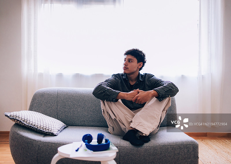 年轻男子在明亮的客厅环境中放松，坐在灰色沙发上图片素材
