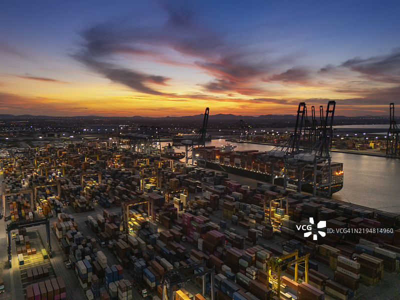 黎明时分的商业港口航拍视图，货柜船停靠，适用于商业物流、进出口、航运或货物运输。图片素材
