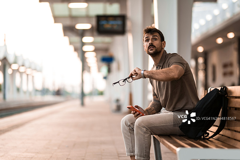担心的男人在火车站等车时查看时间。图片素材